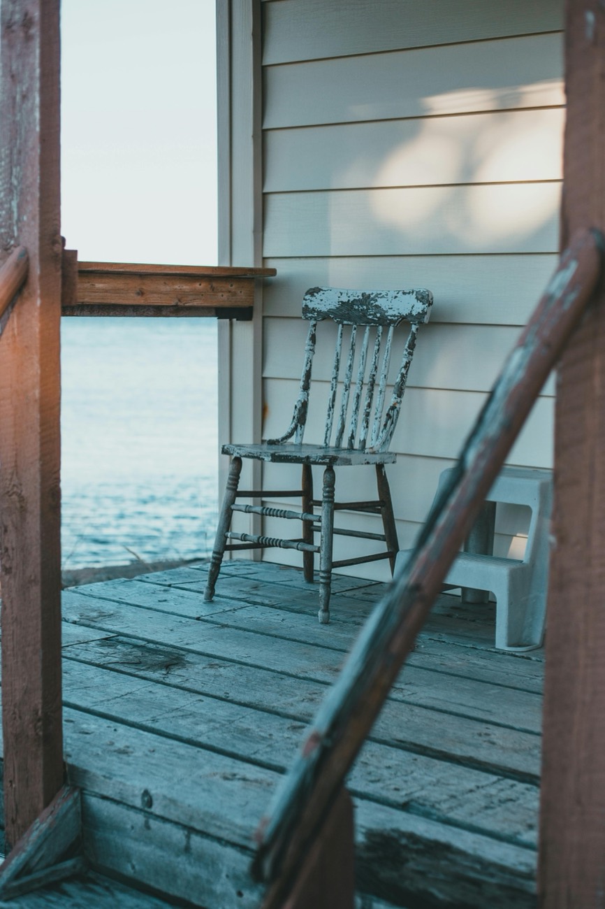 A weathered painted spindle chair on a dock porch, the water beyond