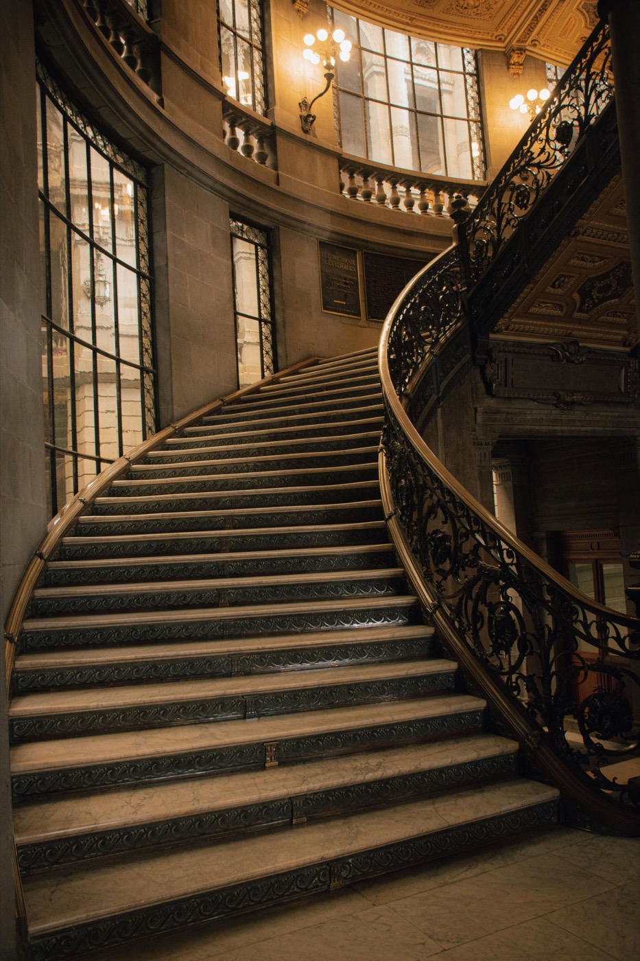 A grand sweeping staircase with an ornate iron balustrade under warm sconce light