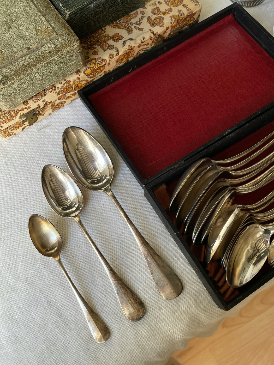 Antique silver spoons laid out beside the open red-felt case and paisley boxes