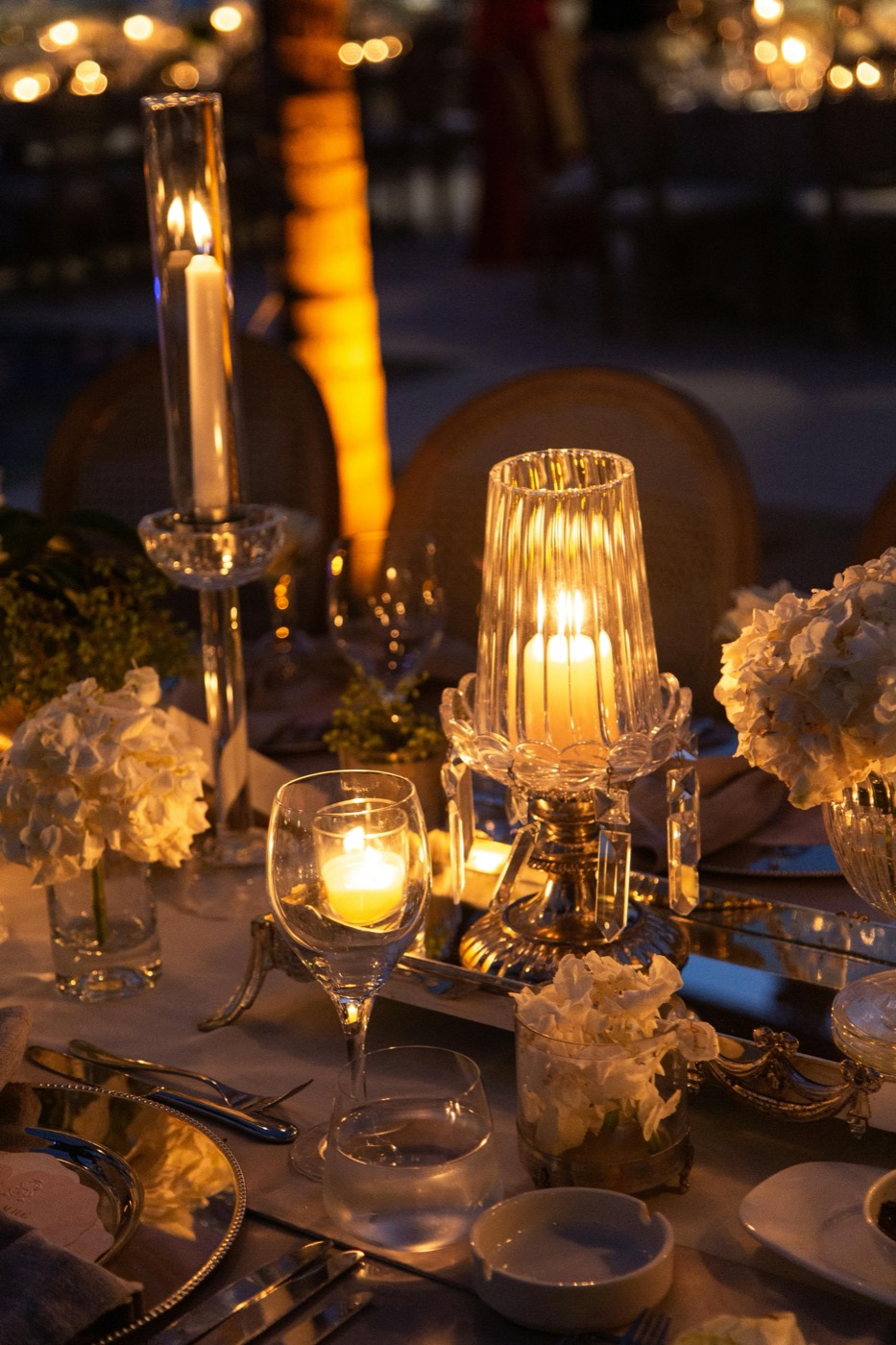 A candlelit night tablescape — hurricane lamps, tapers, white florals, mixed crystal