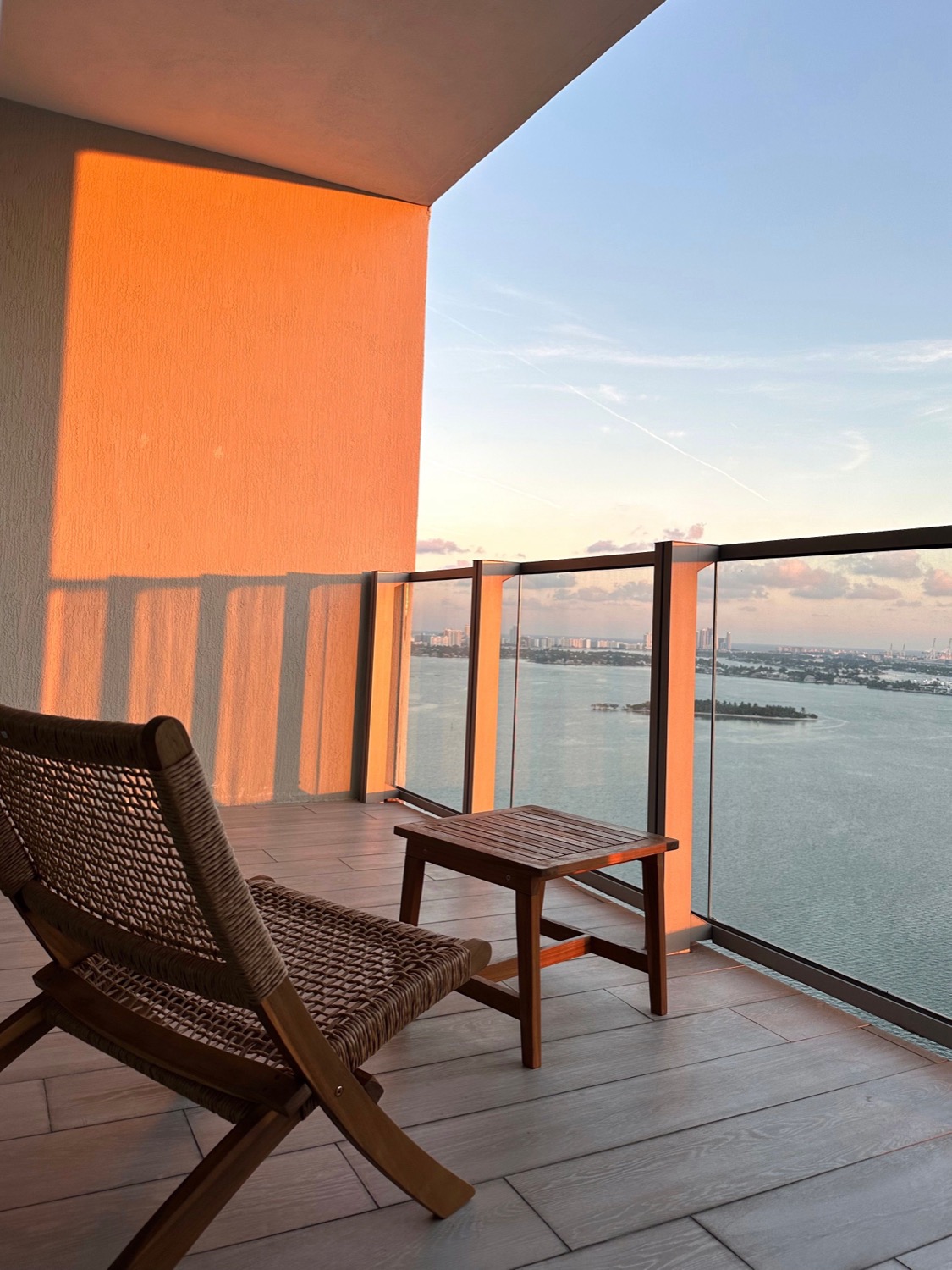 A Miami high-rise terrace at sunset, rattan chair and teak table over Biscayne Bay