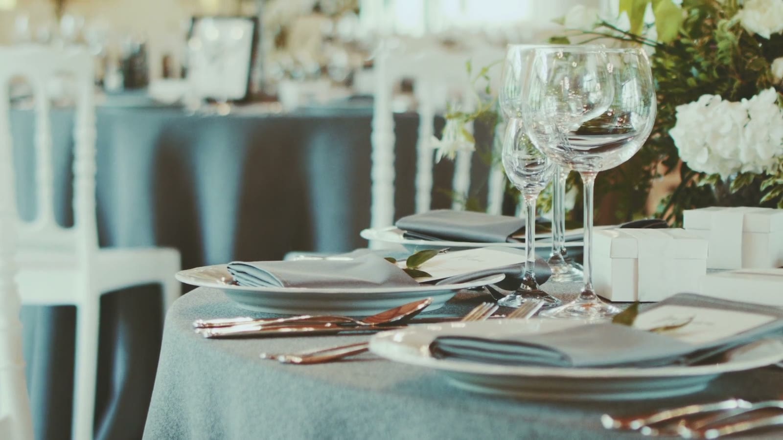 A wedding reception table set with glassware and white flowers, the room beyond softly out of focus