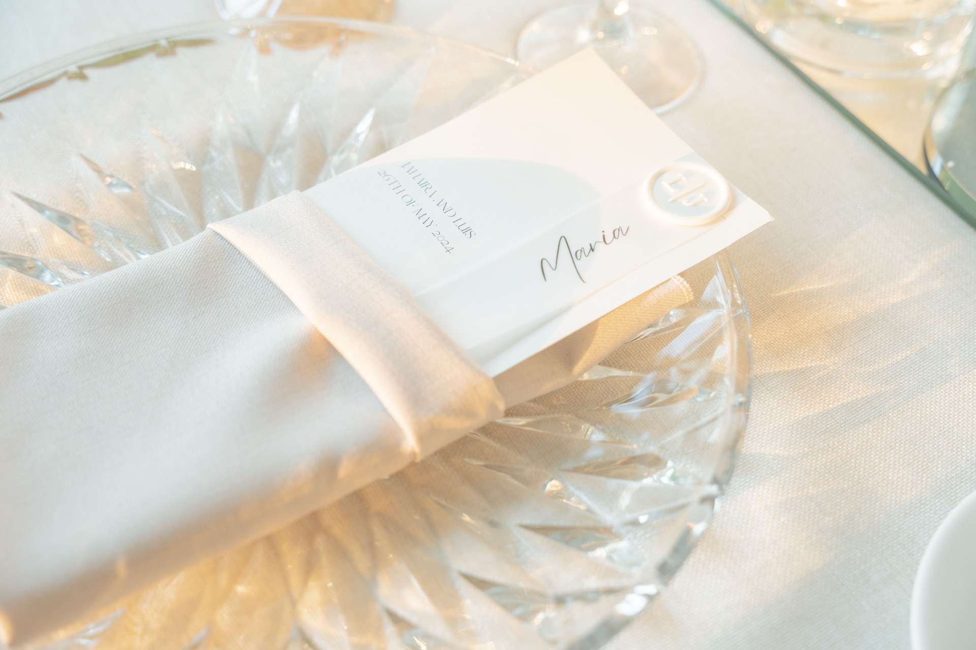 Place card reading Maria tucked into a linen napkin at a softly lit wedding table