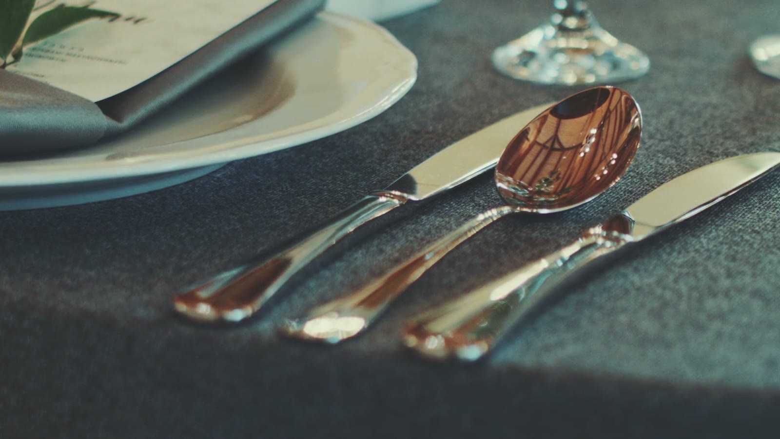Polished silver laid on grey linen beside a plate and menu card, warm light catching the spoon