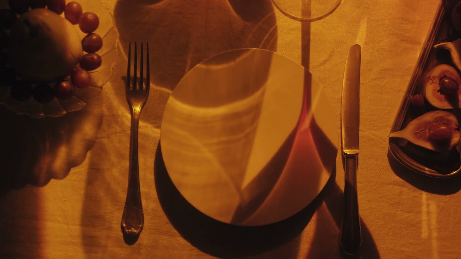 An overhead view of a candlelit dinner setting, warm amber light on plate, silver and glass
