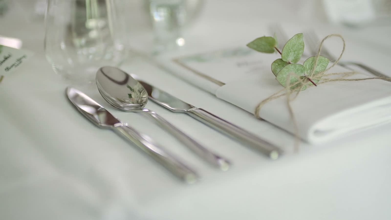 A bright place setting — silver, a menu card, and a sprig of greenery
